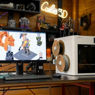 3D printer with computer displaying design on desk.